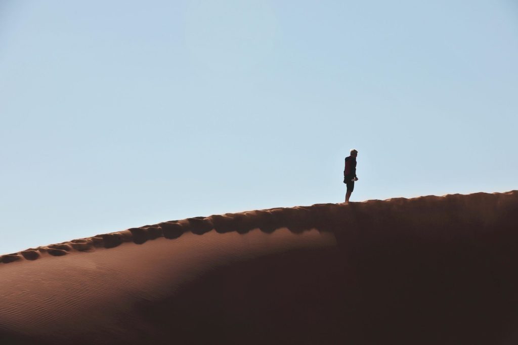 A lone hiker walking on a vast dune at Sossusvlei, Namibia, against a clear sky.